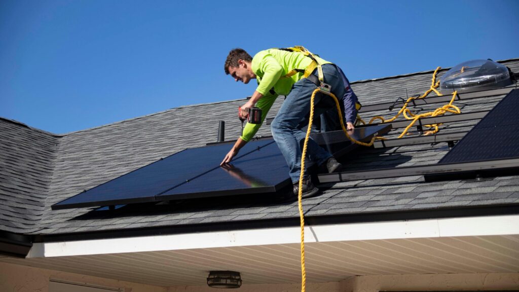 A professional fitting a solar panel on top of a roof of a house.